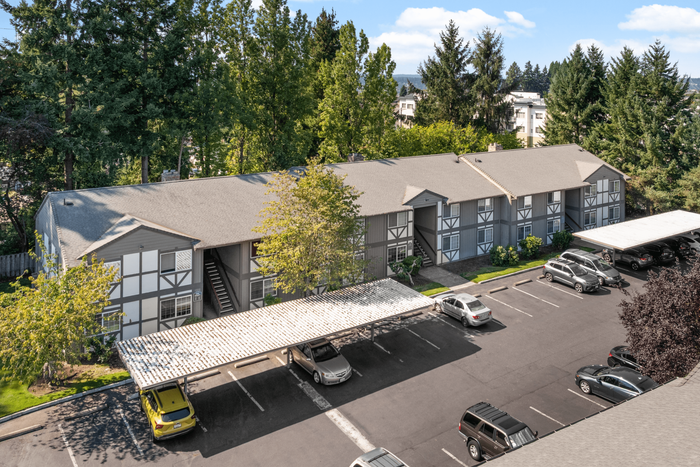 Charming apartment complex surrounded by lush greenery, featuring covered parking and Tudor-style architecture.