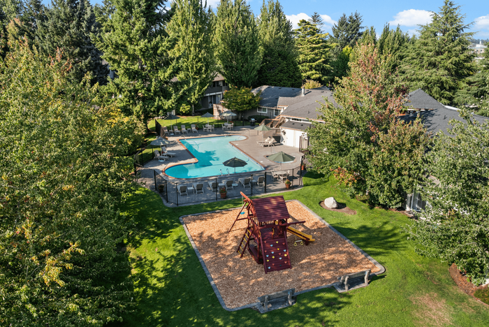 Inviting outdoor space featuring a sparkling pool with lounge chairs, surrounded by lush trees and a vibrant playground area.