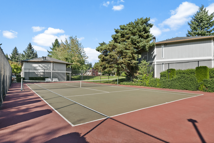 Inviting outdoor tennis court surrounded by lush greenery and charming residences, perfect for recreational enjoyment.