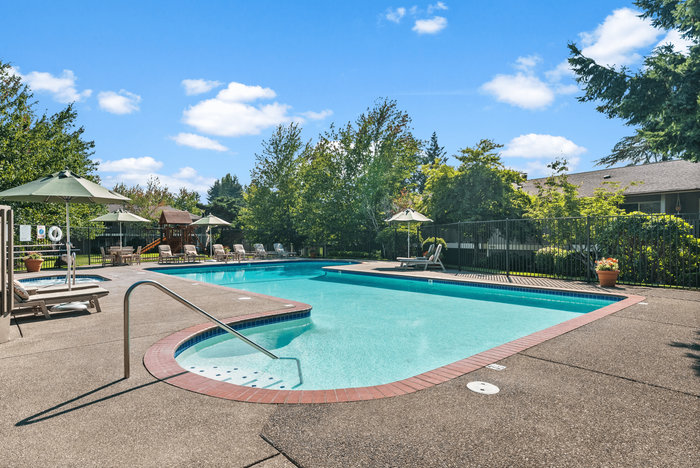 Inviting outdoor swimming pool area with lounge chairs, surrounded by lush greenery and bright blue skies.