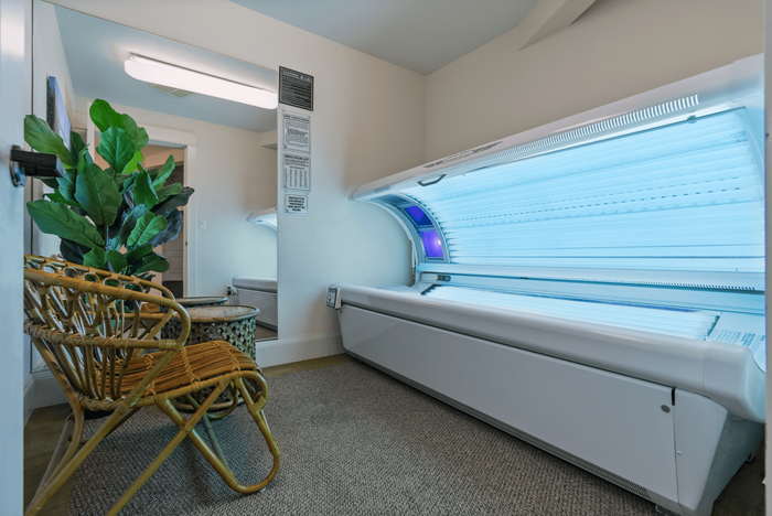 Chic and inviting tanning room with modern tanning bed, stylish wicker chair, and lush green plant, creating a relaxing ambiance.