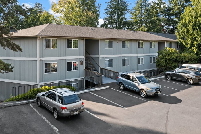 Charming apartment complex with modern design, nestled in a lush green setting, featuring ample parking and inviting pathways.