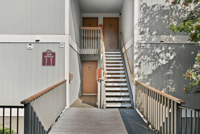 Contemporary apartment entrance with a clean, inviting staircase and wooden railing, surrounded by lush greenery.
