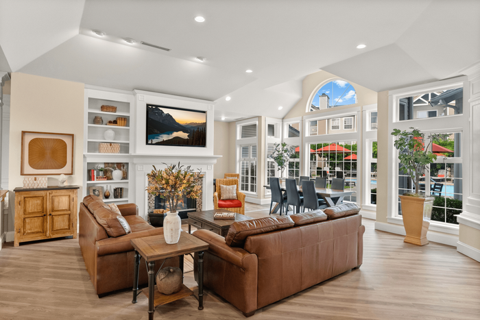 Bright, open living and dining area featuring elegant leather sofas, modern decor, and expansive windows overlooking a lively outdoor space with red umbrellas.