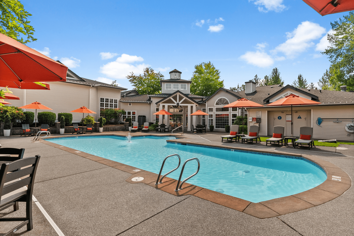 Inviting apartment community with a sparkling swimming pool, surrounded by elegant loungers and vibrant orange umbrellas, perfect for relaxation and leisure.