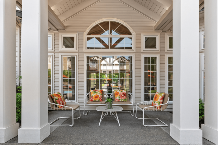 Charming outdoor seating area with vibrant floral cushions, framed by elegant white columns and large windows.
