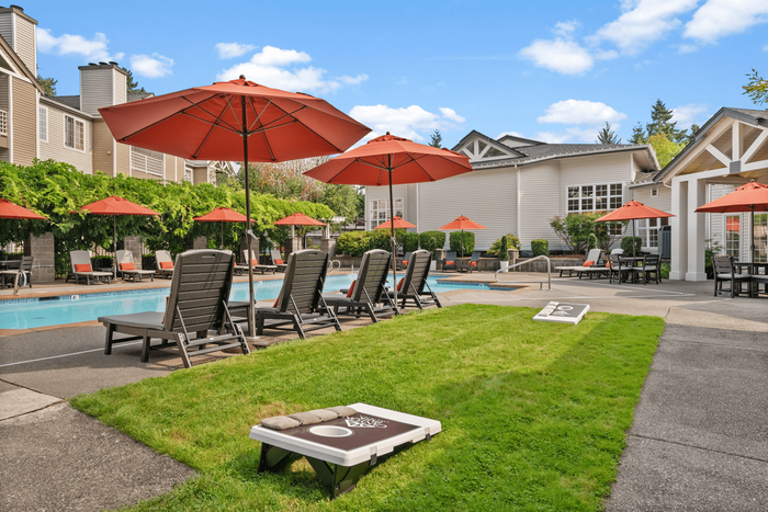 Inviting outdoor area featuring a sparkling pool with sun loungers and vibrant red umbrellas, surrounded by lush greenery and modern architecture.