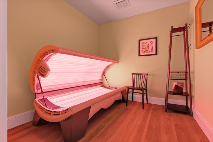 Inviting room featuring a modern tanning bed, wooden chair, and elegant decor, ideal for relaxation and leisure.