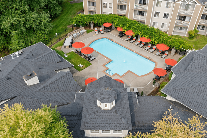 Aerial view of luxurious apartment complex featuring an inviting swimming pool surrounded by vibrant red umbrellas and lush greenery.
