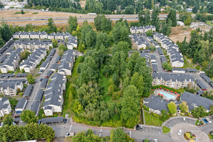 Aerial view of a charming apartment complex surrounded by lush greenery and landscaped gardens, featuring inviting pathways and a pristine community swimming pool with red umbrellas.