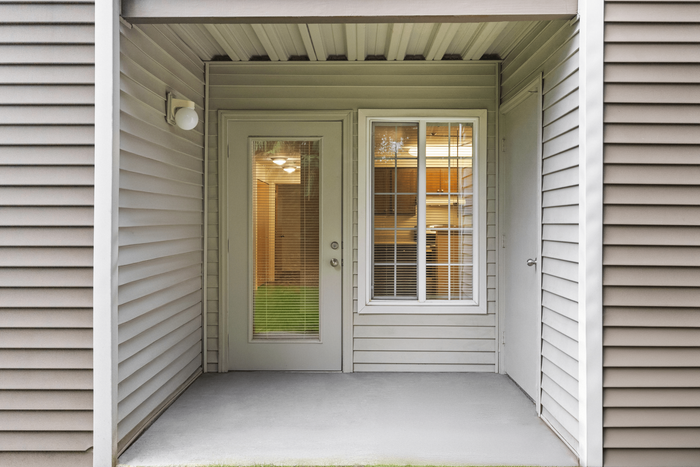 Inviting apartment entrance featuring elegant siding and large window panels with blinds, offering a glimpse into a cozy, illuminated interior.