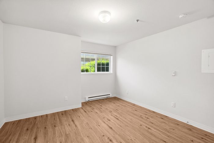 Bright and inviting empty room featuring elegant wood flooring, a modern light fixture, and a large window with abundant natural light.