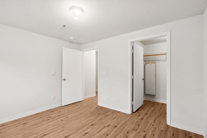 Bright, freshly painted room with elegant wooden flooring, featuring two open doors and a spacious closet, ideal for a modern, minimalist lifestyle.