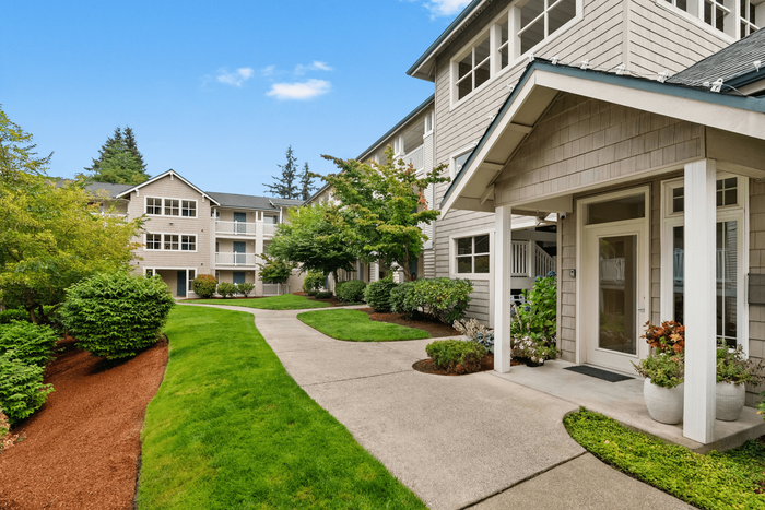Charming apartment building with lush green landscaping, vibrant shrubs, and a welcoming entrance, perfect for tranquil living.
