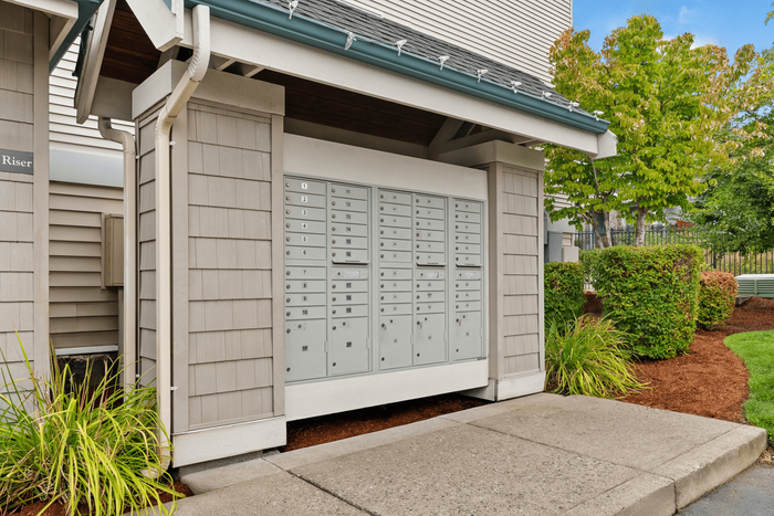 Charming apartment mail center with organized mailboxes, surrounded by lush greenery and modern architecture.
