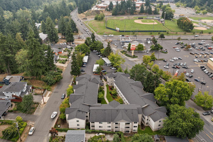 Aerial view of a charming apartment complex nestled amidst lush greenery, with convenient proximity to shops and recreational facilities.