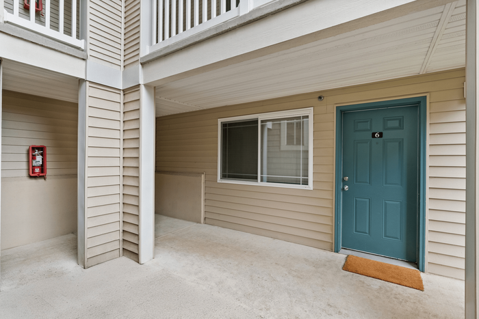 Inviting apartment entrance with a teal door, welcome mat, and covered patio area, perfect for cozy entryway ambiance.