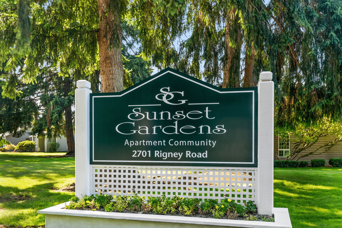 Welcoming sign of Sunset Gardens Apartment Community nestled among lush green trees, showcasing a serene and inviting atmosphere.