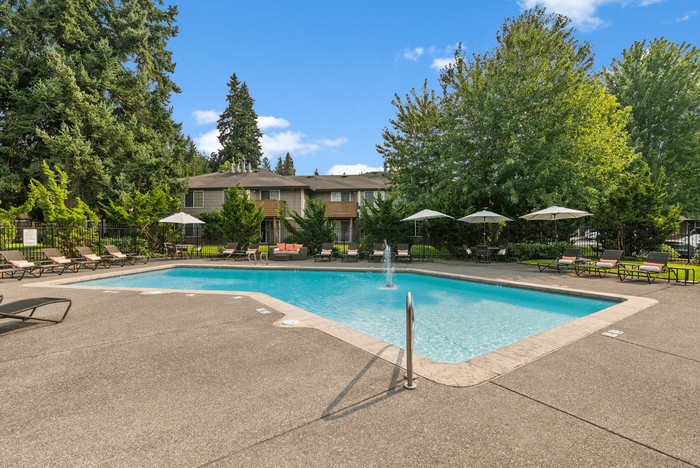 Inviting outdoor pool with lounge chairs and umbrellas surrounded by lush greenery, perfect for relaxation.