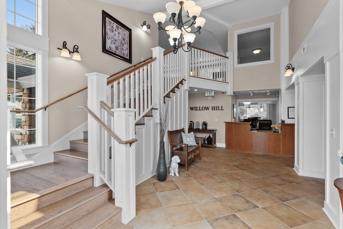 Elegant lobby of Willow Hill featuring a grand staircase, stylish chandelier, and welcoming seating area, exuding charm and sophistication.