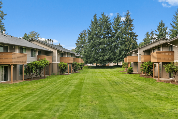 Charming apartment complex with spacious balconies, lush green lawns, and towering trees, offering serene suburban living.