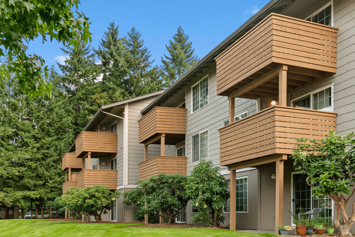 Charming apartment building with private wooden balconies, surrounded by lush greenery and tall trees.
