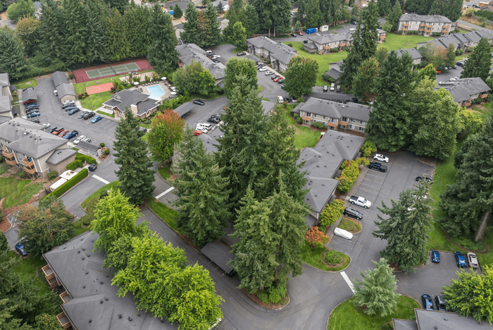 Charming apartment complex nestled in lush greenery, featuring ample parking, a tennis court, and a swimming pool for vibrant community living.