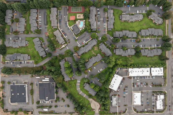 Vibrant aerial view of a spacious apartment complex with lush greenery, ample parking, and recreational facilities including a pool and tennis court.