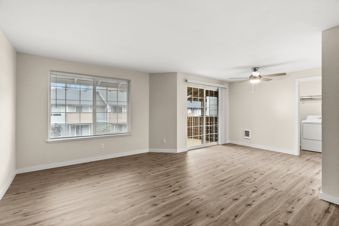 Bright and airy living space with elegant wood flooring, large window views, and a modern ceiling fan, leading to a cozy balcony with sliding glass doors.