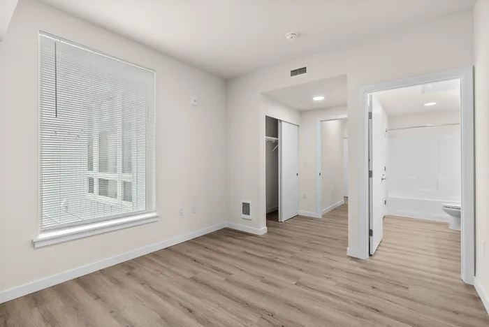 Bright and airy bedroom with modern wood flooring, large window with blinds, and convenient access to an en-suite bathroom.