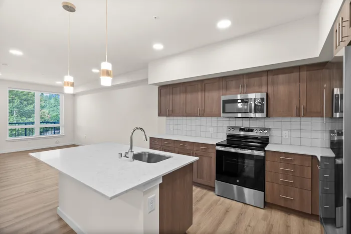 Modern open-concept kitchen with elegant wood cabinets, stainless steel appliances, and a sleek island, offering a bright and spacious living area with large windows and scenic views.