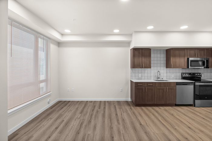 Modern apartment interior showcasing a sleek kitchen with stainless steel appliances, elegant wooden cabinetry, and large bright windows with blinds.
