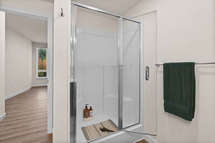 Elegant bathroom featuring a sleek glass shower with chrome accents and modern wood flooring, offering an inviting and bright atmosphere.