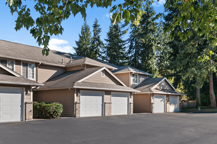Charming townhouse complex with attached garages nestled among lush, tall trees, offering a serene suburban vibe.