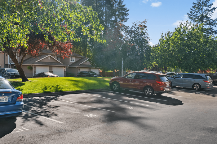 Charming suburban scene showcasing a lush, green lawn and modern townhouses framed by vibrant trees, with ample parking space in a serene neighborhood setting.