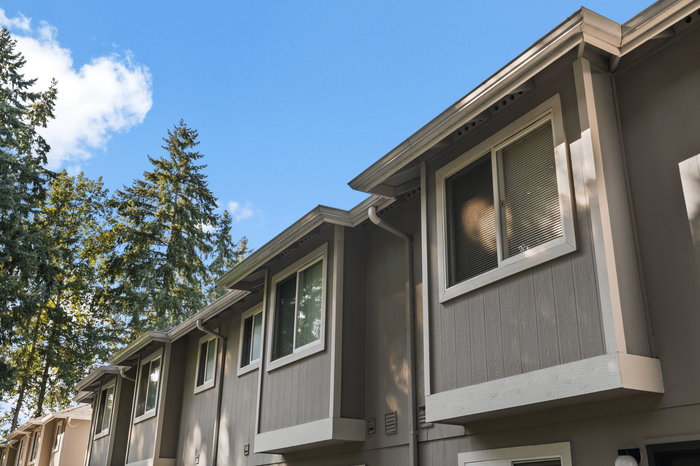 Charming townhouse exterior showcasing modern design with large windows and lush trees in the background.