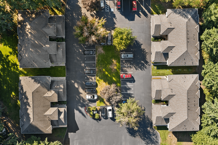 Aerial view of a picturesque apartment complex surrounded by lush greenery, showcasing ample parking space and well-maintained pathways.