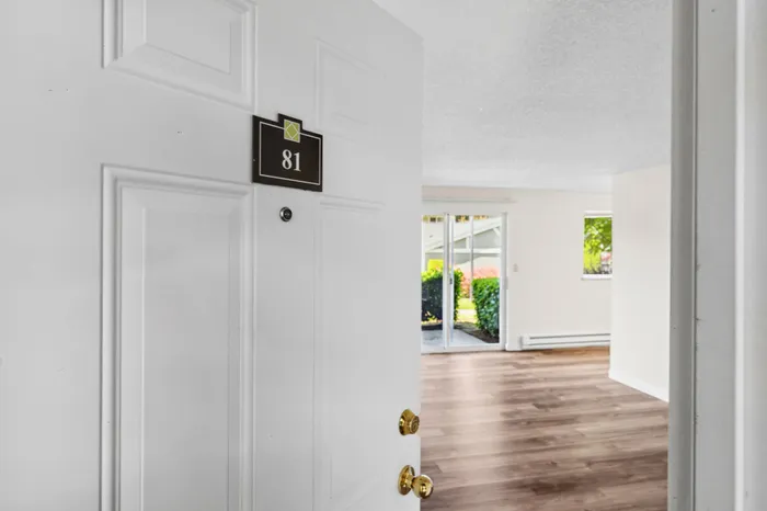 Welcoming entry to a bright, spacious apartment featuring modern hardwood floors and a serene view through large sliding glass doors.