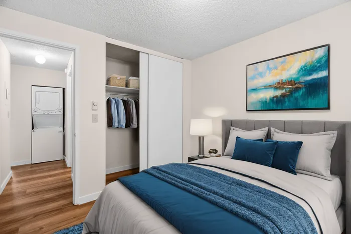 Inviting bedroom with elegant decor, featuring a cozy bed with plush blue accents, a spacious closet, and convenient in-unit laundry.
