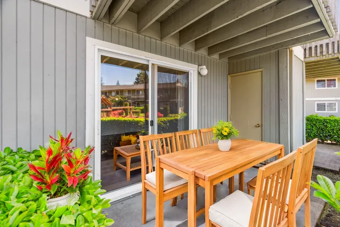 Charming patio with elegant wooden dining set, vibrant plants, and serene garden views, perfect for outdoor relaxation.