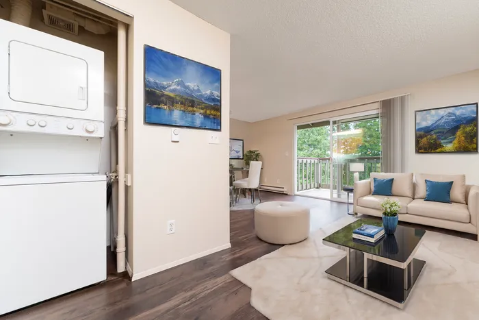 Inviting living room with plush seating, elegant artwork, and access to a private balcony. Featuring a convenient in-unit washer and dryer for modern living.