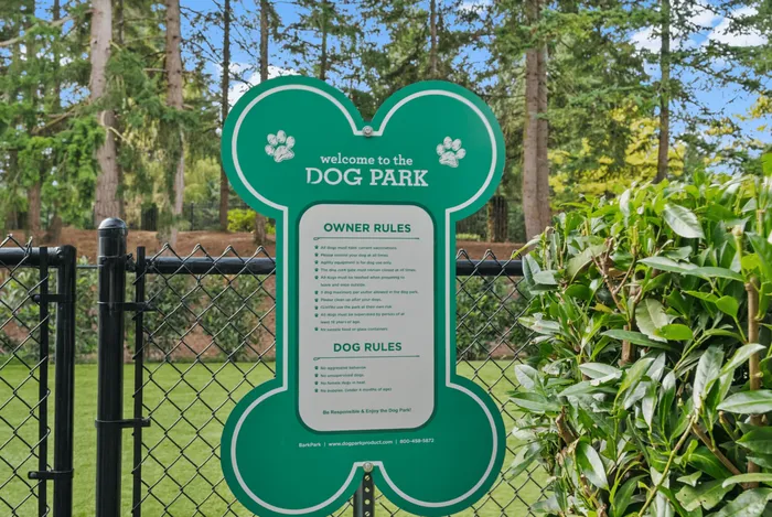 Lush dog park entrance with welcoming sign shaped like a bone, surrounded by vibrant greenery and tall trees.
