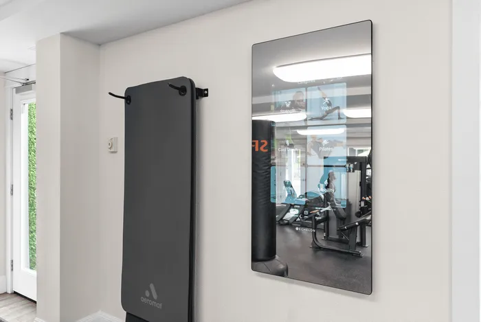Smart fitness mirror with touch display and mounted exercise mat in a modern gym setting.