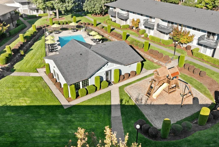 Charming apartment complex featuring a sparkling pool, vibrant green landscaping, and a fun children's playground.