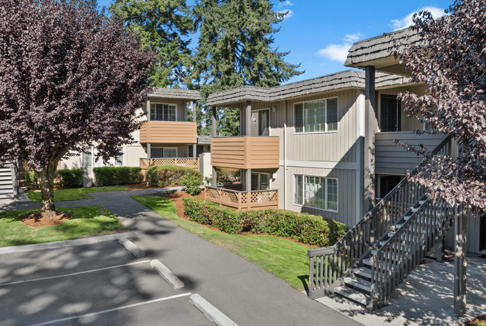 Charming apartment complex with modern balconies, surrounded by lush greenery and sunlit pathways.