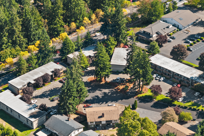 Aerial view of a charming apartment complex surrounded by lush greenery and vibrant autumn colors, offering tranquil living with convenient parking.