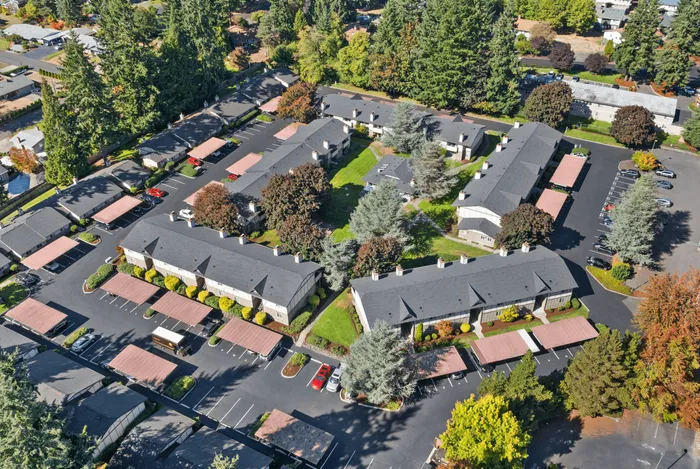 Aerial view of a charming apartment complex surrounded by lush greenery and well-maintained landscapes, featuring ample parking and spacious courtyards.