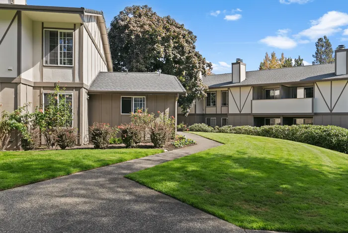 Charming apartment complex with manicured lawns and lush greenery, bathed in bright sunlight, perfect for serene living.