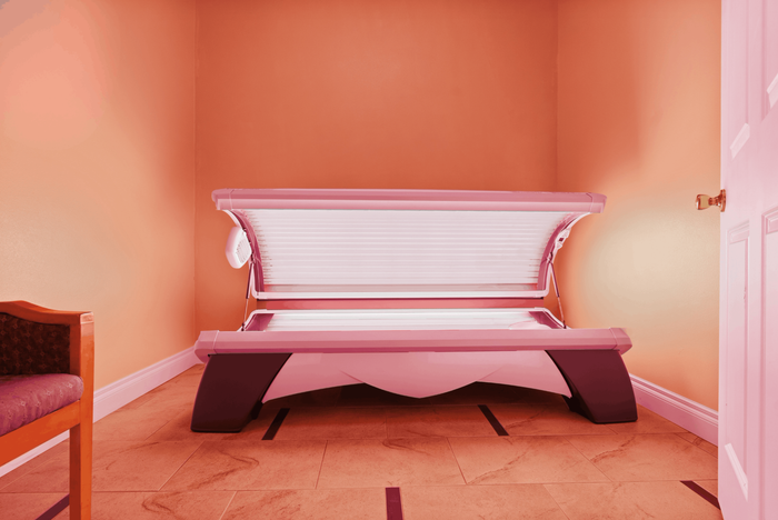 Inviting wellness space with a sleek pink high-tech tanning bed and warm orange-toned walls for ultimate relaxation.