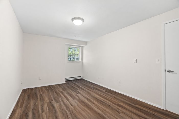 Bright and spacious room featuring sleek wood flooring and large window, ideal for versatile living space.